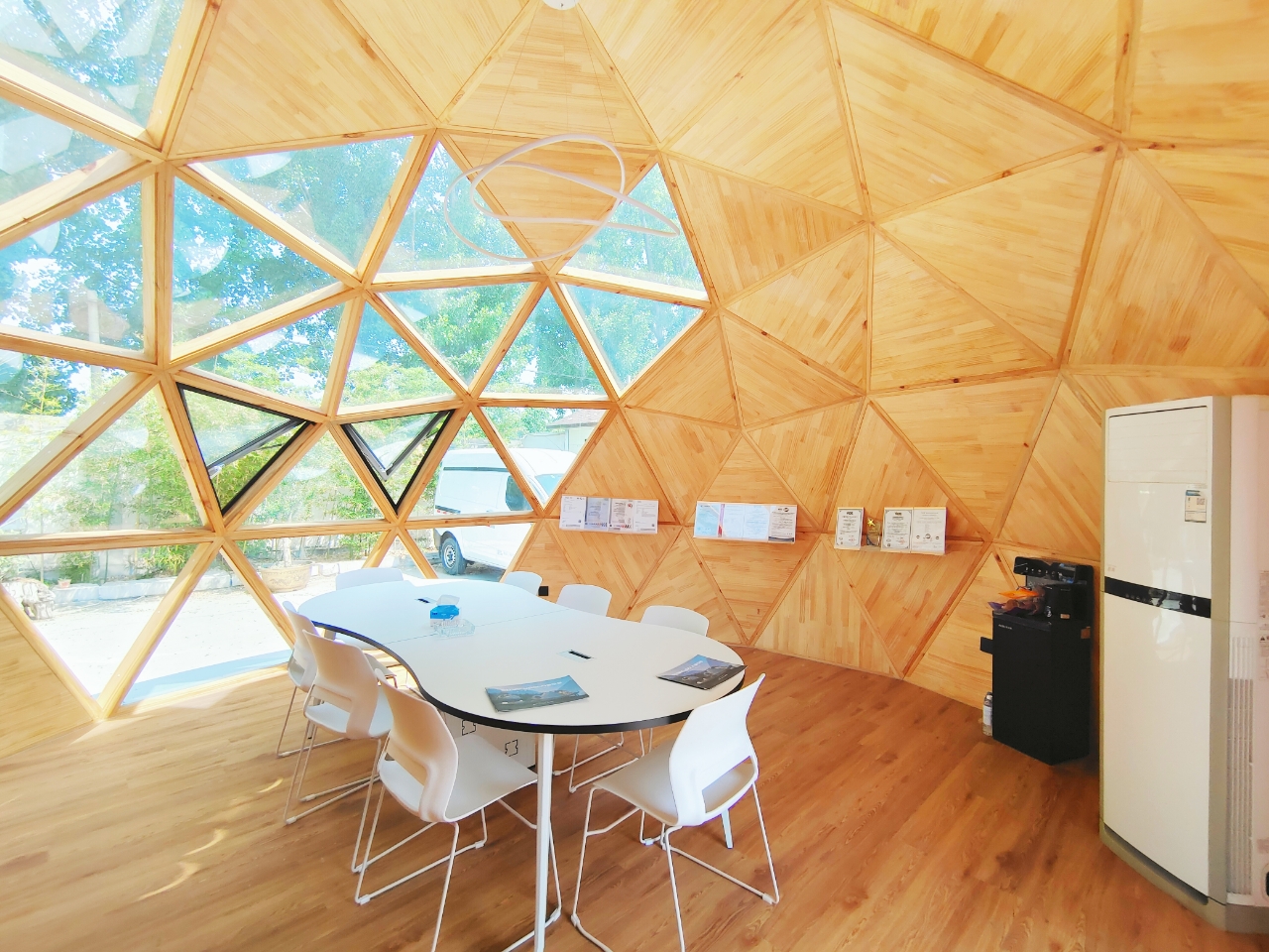 Bright interior of the bahria homes House C7 Plus with wooden geodesic dome panels, large glass windows, and a minimalist meeting setup featuring a white table and chairs.