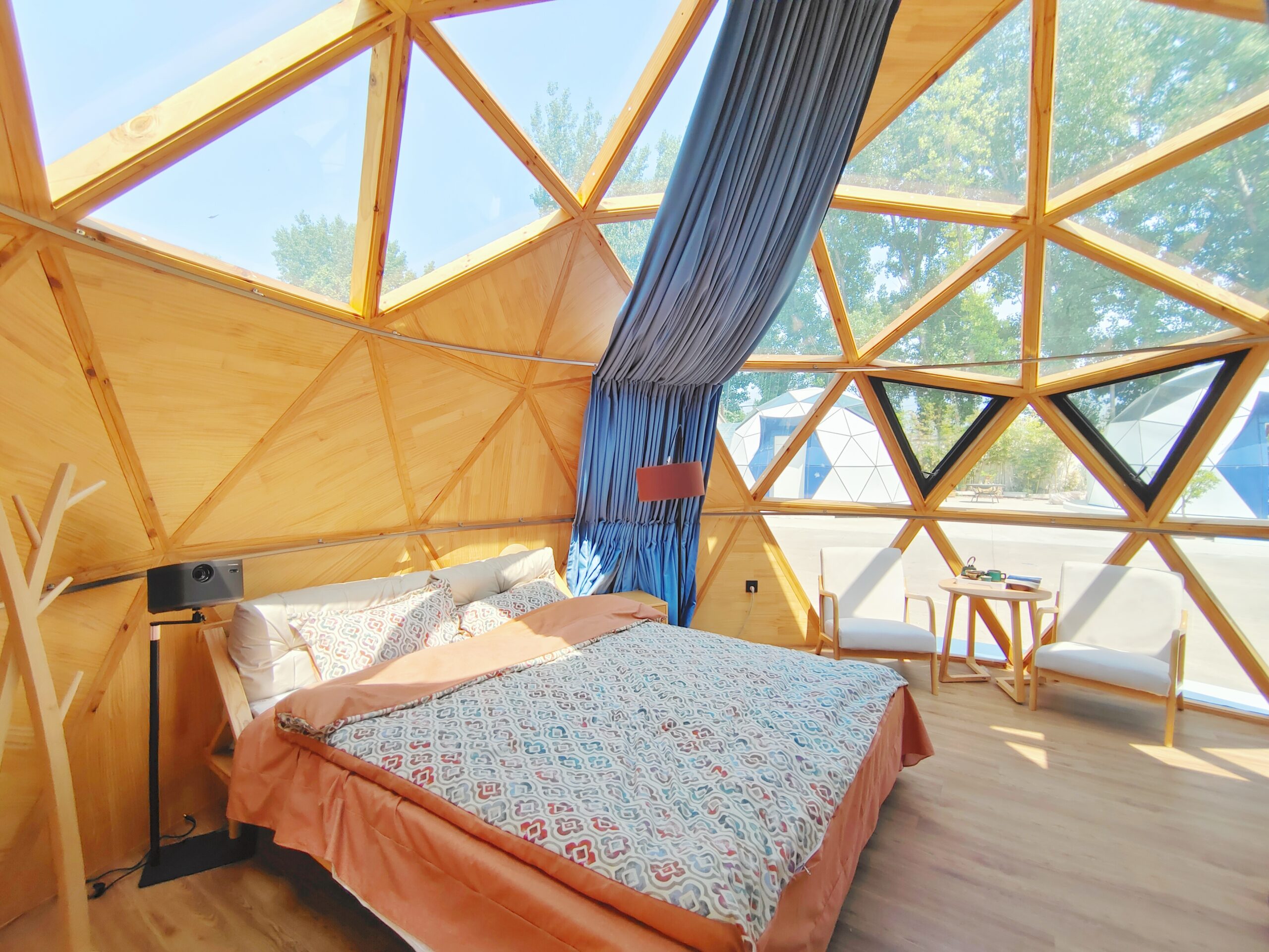 Interior of the bahria homes House C7 Plus featuring a modern wooden geodesic dome structure with a bed, chairs, and panoramic glass windows offering natural light and outdoor views.