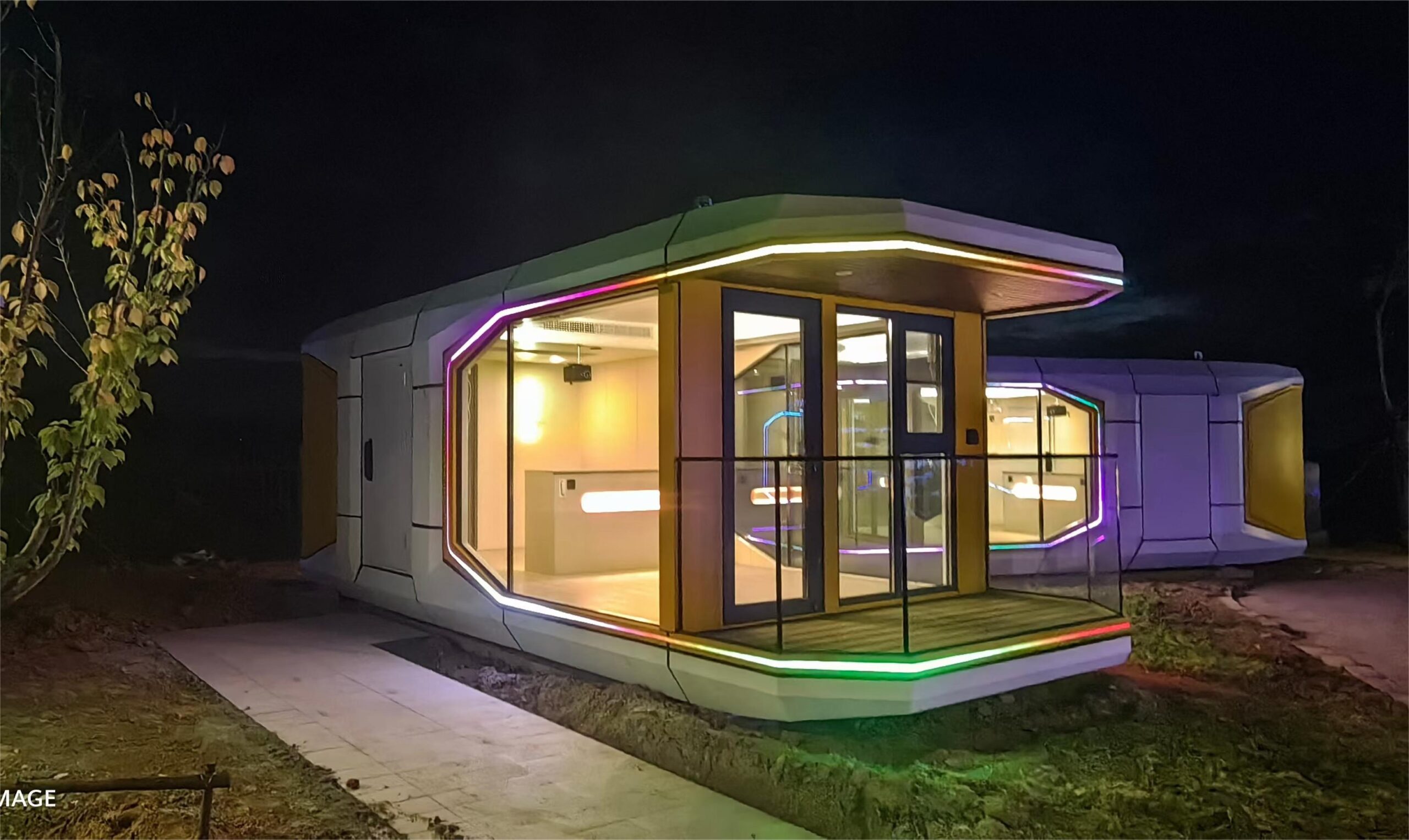 Night view of the bahria homes House modular smart pod illuminated with colorful LED lights, featuring large glass panels and modern geometric architecture.