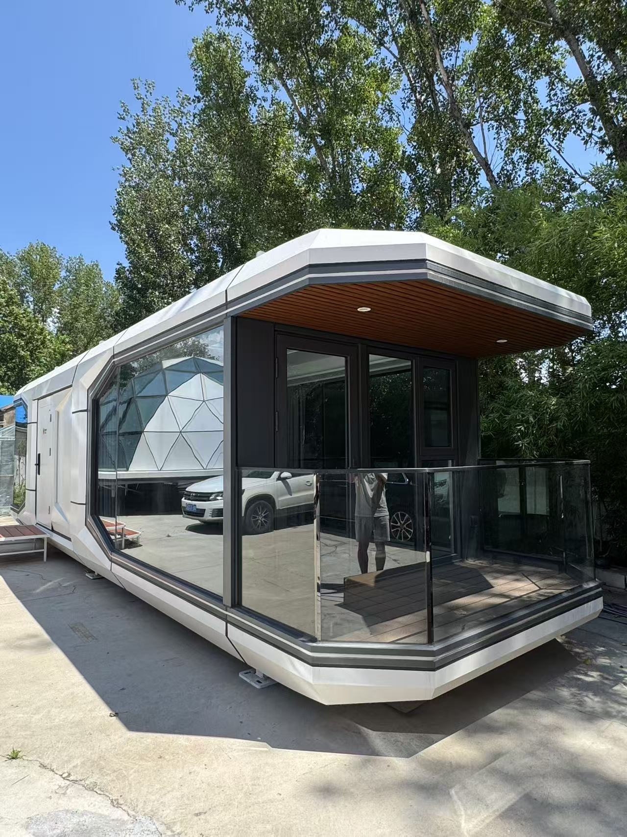 Front view of the bahria homes House D7 modular smart pod featuring large glass walls, a compact balcony, and futuristic white geometric architecture under a clear sky.