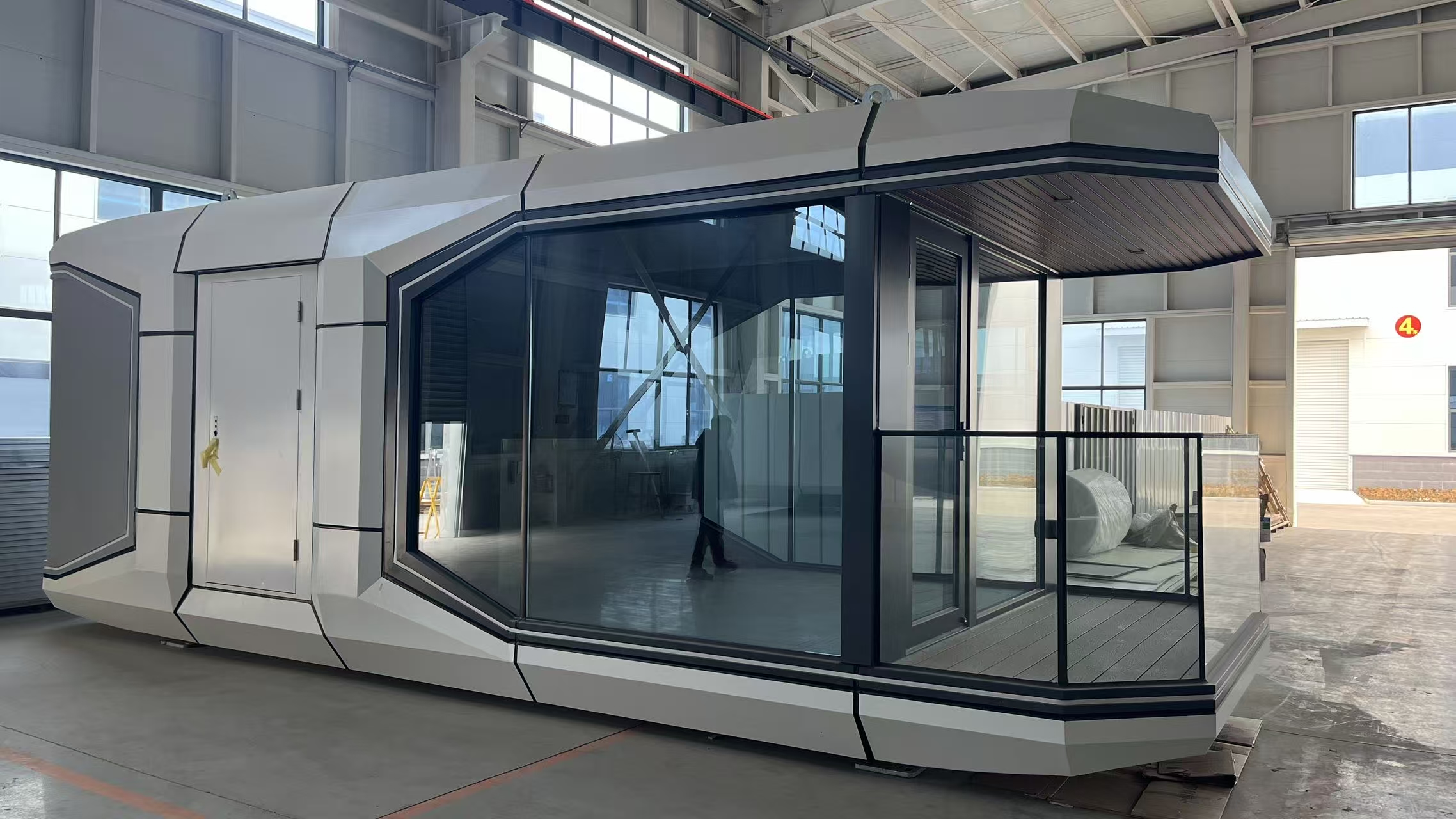 Newly assembled bahria homes House modular smart pod with sleek geometric design, large glass walls, and balcony area inside a production facility.