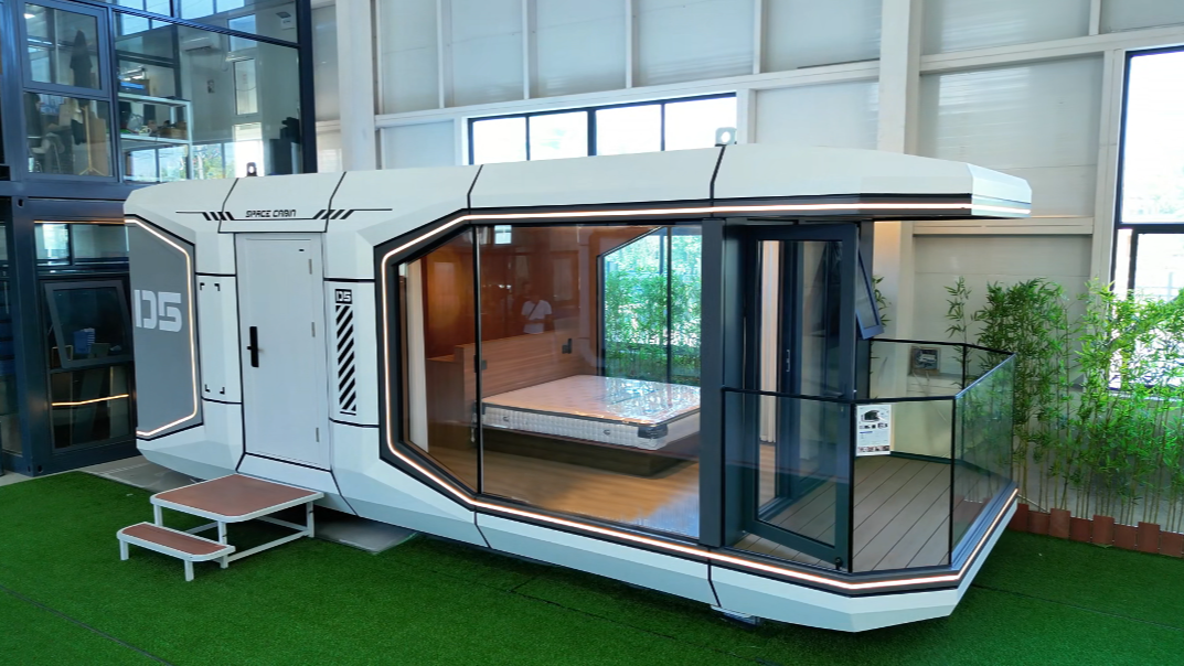 bahria homes House D5 modular smart pod with sleek white exterior, large glass windows, balcony area, and interior bedroom setup displayed in a modern indoor showroom.