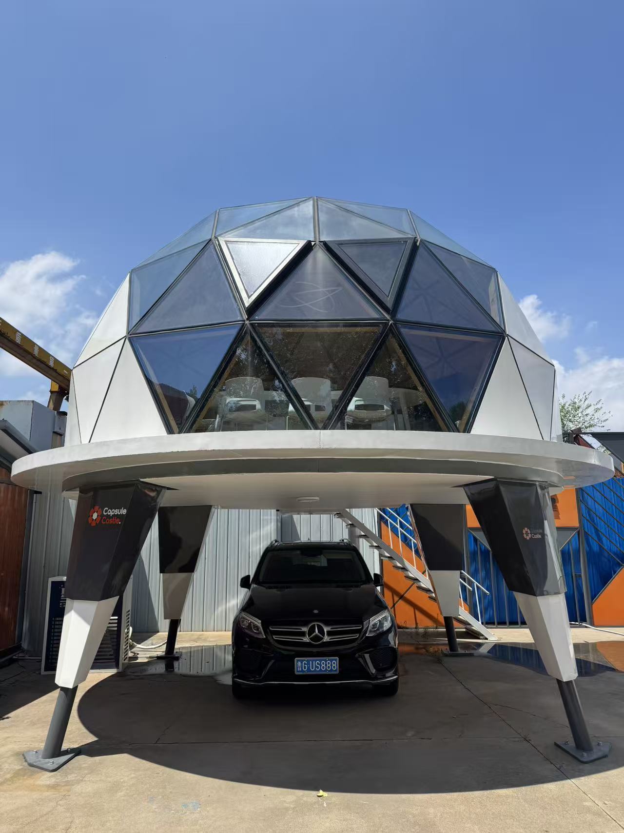 Front view of the bahria homes House C7 Plus elevated geodesic dome with glass panels and metal supports, featuring a car parked beneath under clear blue skies.